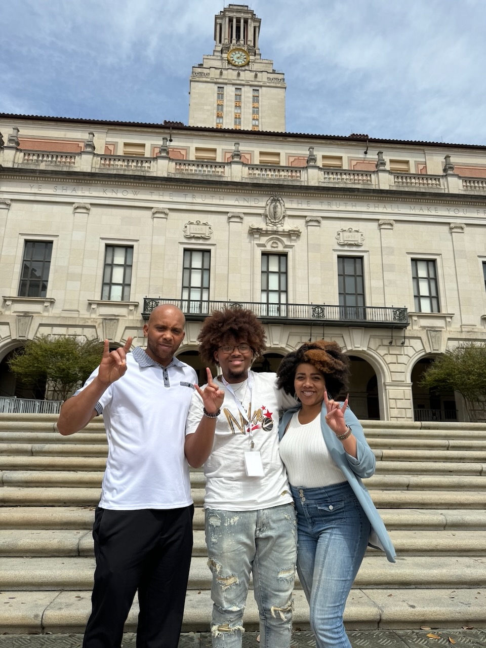 Three people pose in front of a large building outside. They are all holding up the hang loose sign.